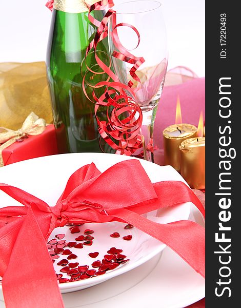 New Year's or Valentine's setting - a plate decorated with ribbon and heart shaped confetti, a bottle of champagne, a glass, candles, a gift in close up