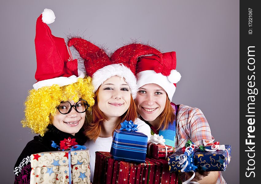 Three girlfriends in funny hats with christmas gifts. Studio shot.