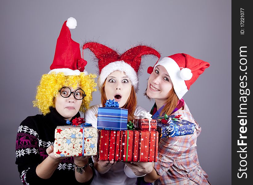 Three girlfriends in funny hats with christmas gifts. Studio shot.