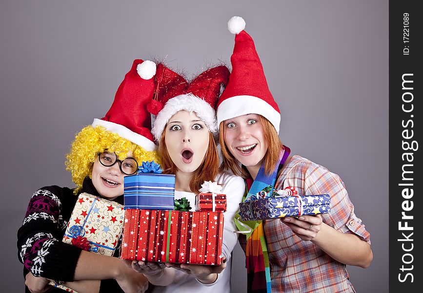 Three girlfriends in funny hats with christmas gifts. Studio shot.