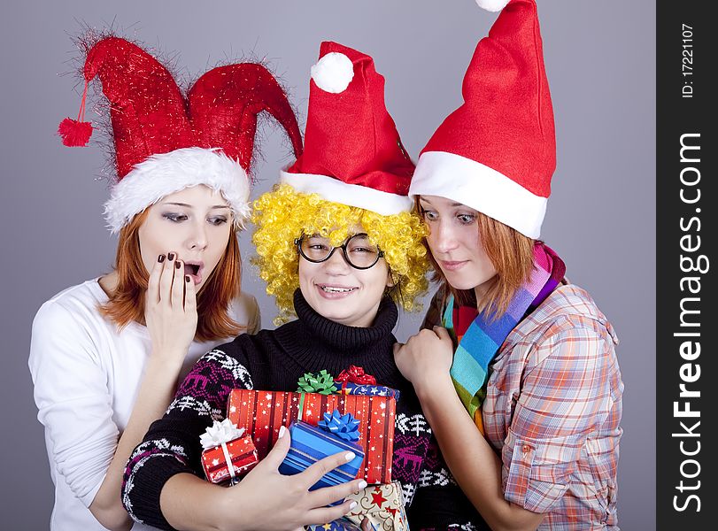 Three girlfriends in funny hats with christmas gifts. Studio shot.