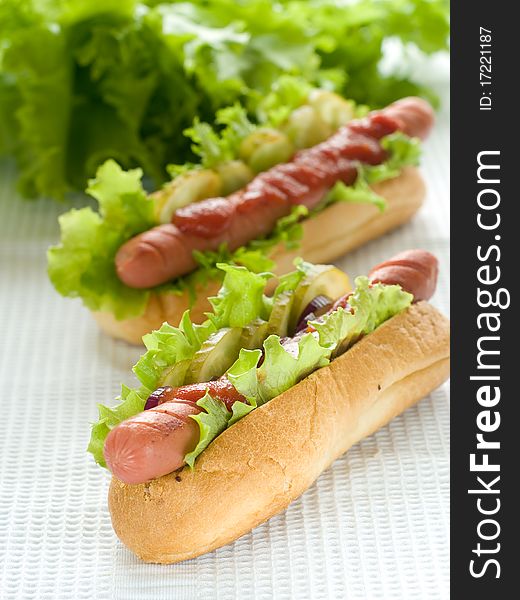 Two hot dogs with sausage, lettuce, ketchup and salted cucumber