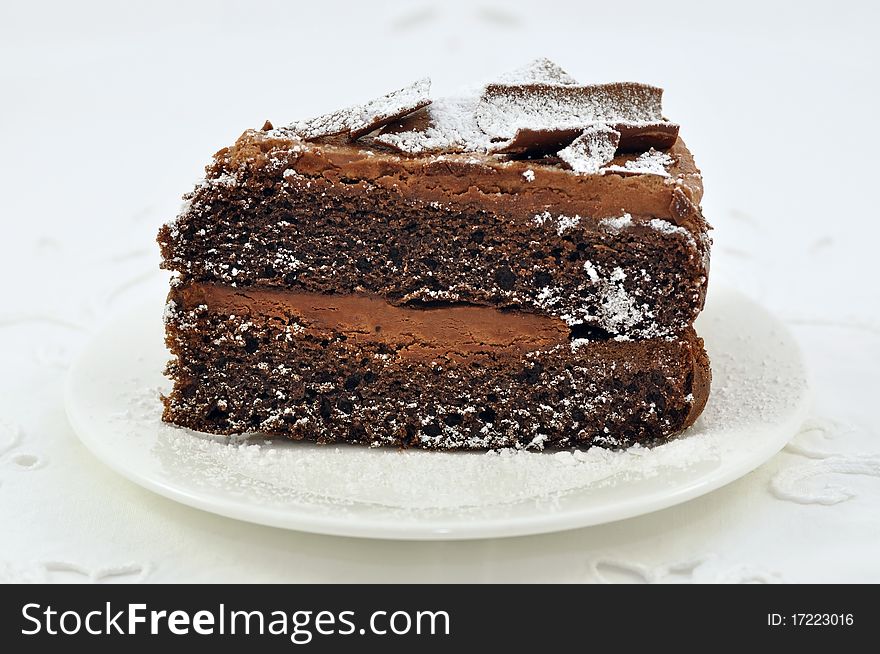 Slice of chocolate cake with white frosting,on white lace tablecloth.