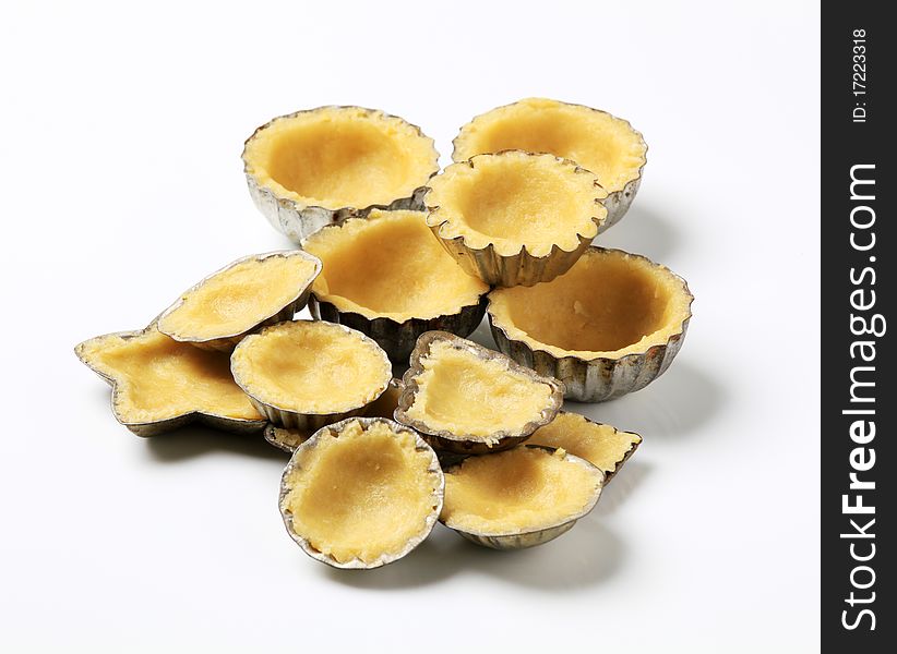 Raw dough in small fluted tartlet pans. Raw dough in small fluted tartlet pans