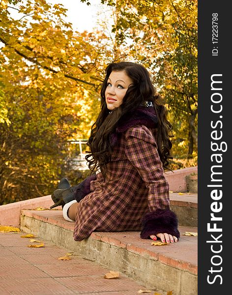 Beautiful glamour girl sits on the stair between fallen leaves