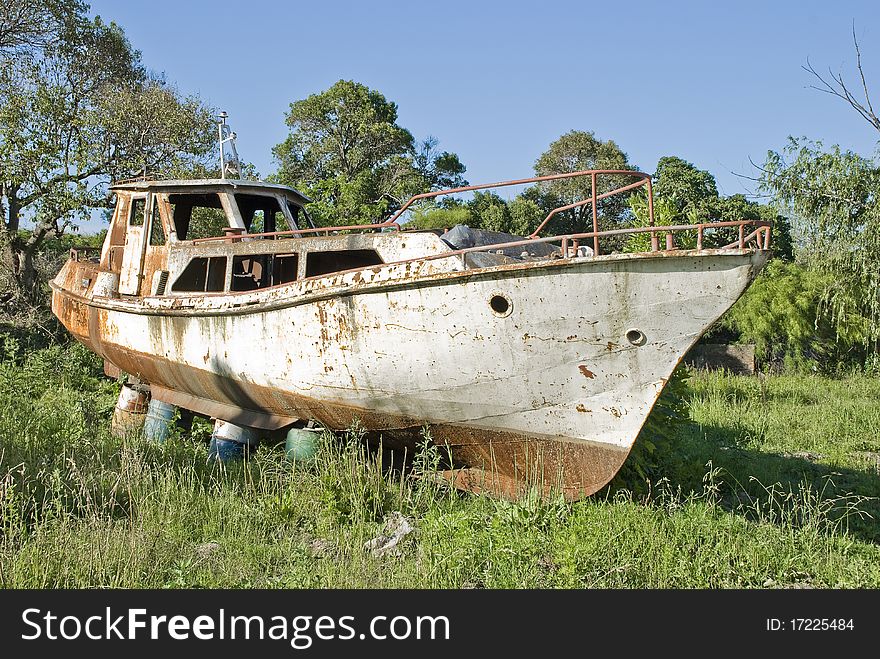 A rusty boat leaning on barrels on the grass, with trees, weeds and a blue sky in the background. A rusty boat leaning on barrels on the grass, with trees, weeds and a blue sky in the background