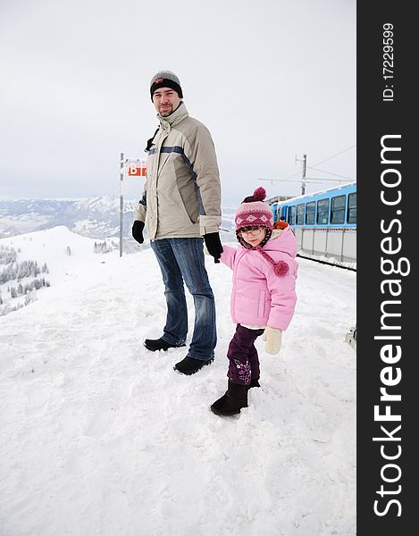 Young father and his daughter in mountains near train in snow winter day