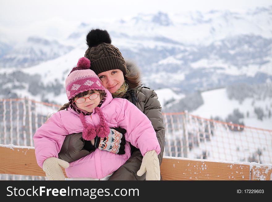 Young mother and daughter in winter mountains looks into the camera