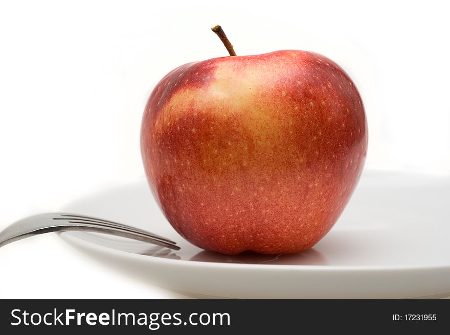 Big red Apple falls on a white plate with cutlery closeup on a white background. Big red Apple falls on a white plate with cutlery closeup on a white background