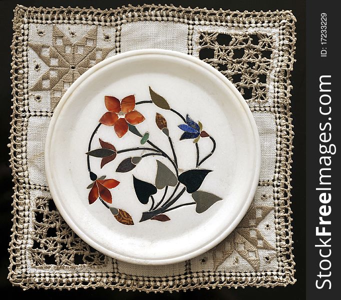 Indian marble plate inlaid of semi precious stones showing flowers. Put on an embroidered  doily. Indian marble plate inlaid of semi precious stones showing flowers. Put on an embroidered  doily