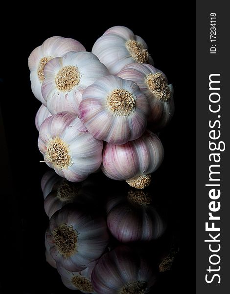 A string of garlic bulbs reflected on a shiny black surface