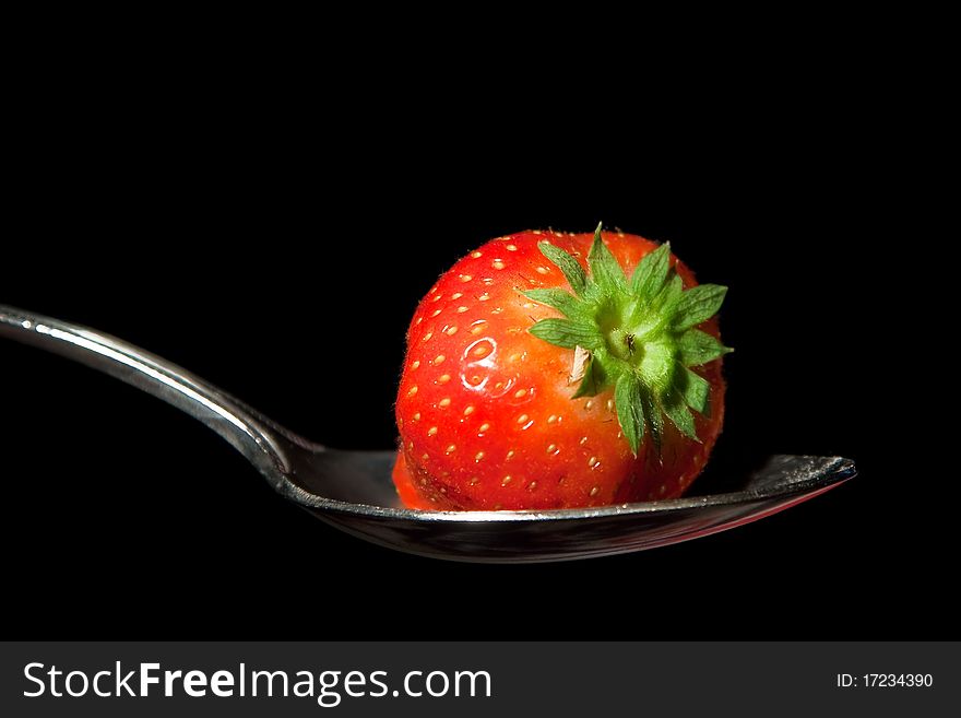 A single strawberry on a metal spoon against a black background