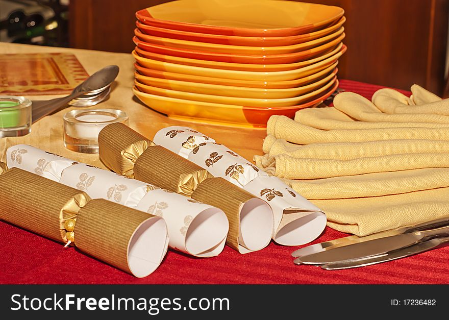 Christmas crackers, napkins, silverware, and stack of plates on a red tablecloth set the mood for a holiday celebration. Christmas crackers, napkins, silverware, and stack of plates on a red tablecloth set the mood for a holiday celebration.