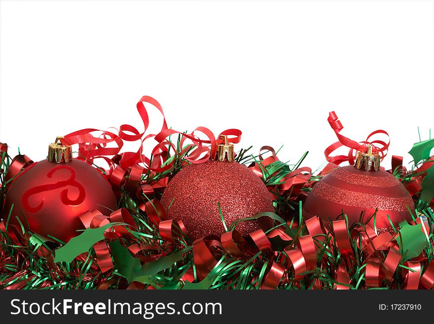 Three red Christmas baubles on green tinsel isolated on white background with copy space.