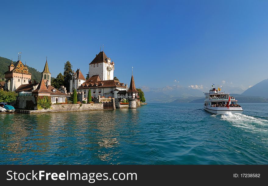 The white tour vessel is passing by a beautiful estate on the coast, against a background of blue sunlighted sky. The white tour vessel is passing by a beautiful estate on the coast, against a background of blue sunlighted sky.