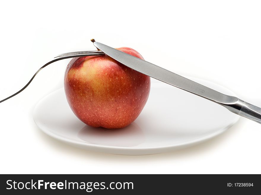 Big red Apple falls on a white plate with cutlery closeup on a white background. Big red Apple falls on a white plate with cutlery closeup on a white background