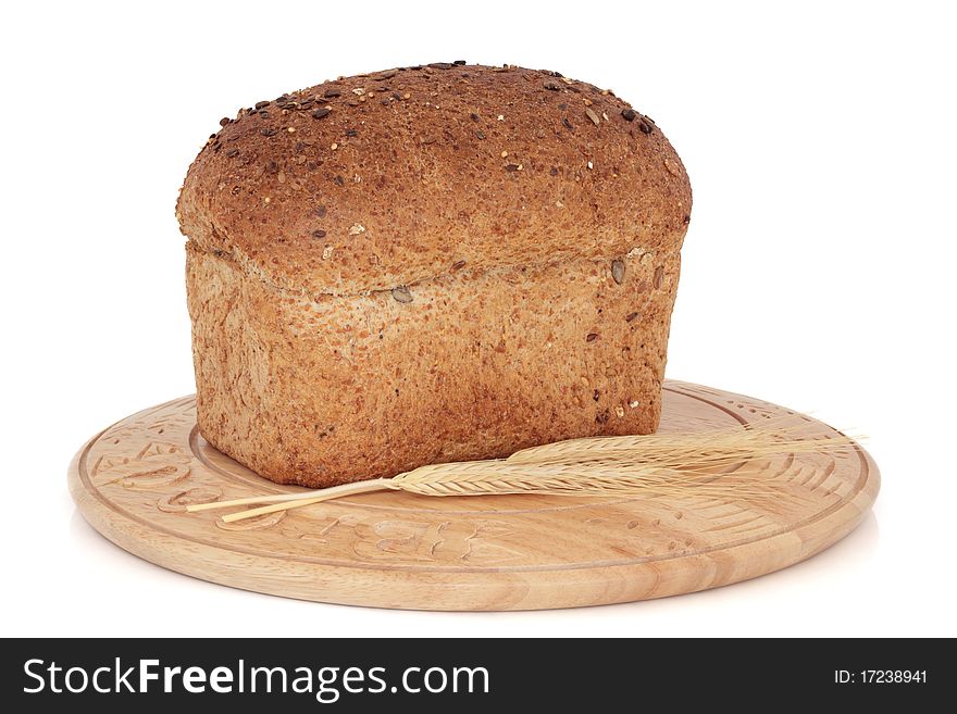 Wholegrain brown bread loaf on a carved rustic bread board with wheat ears isolated over white background. Wholegrain brown bread loaf on a carved rustic bread board with wheat ears isolated over white background.