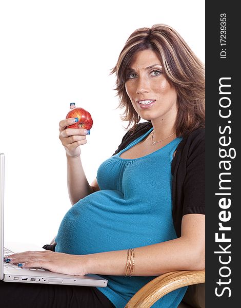 A pregnant business woman sitting and working on her lap top while eating fruit. A pregnant business woman sitting and working on her lap top while eating fruit.