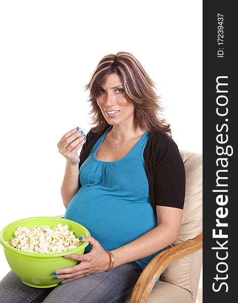 A pregnant woman sitting down eating some popcorn with a happy expression on her face. A pregnant woman sitting down eating some popcorn with a happy expression on her face.