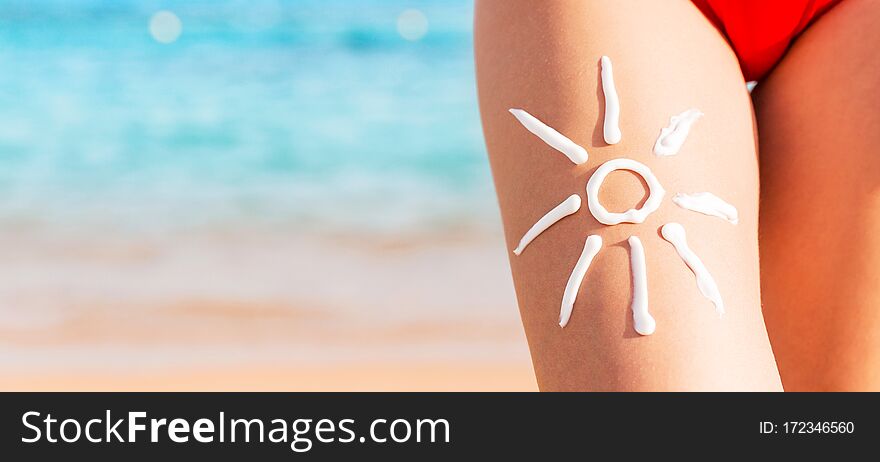 Sun shape is made of sunscreen on woman`s leg at the sea background