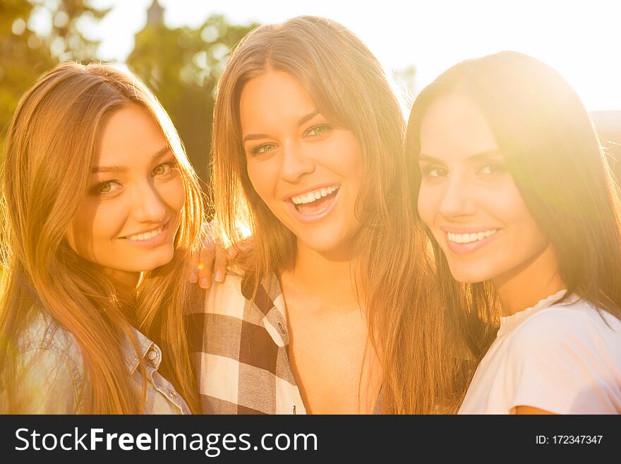 Three smiling joyful girlfriends hugging and looking at camera.