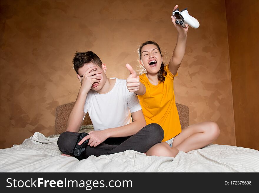 The teenager is upset that he lost a computer game to his sister, covers his face with his palm. In their hands they hold modified joysticks without identification marks