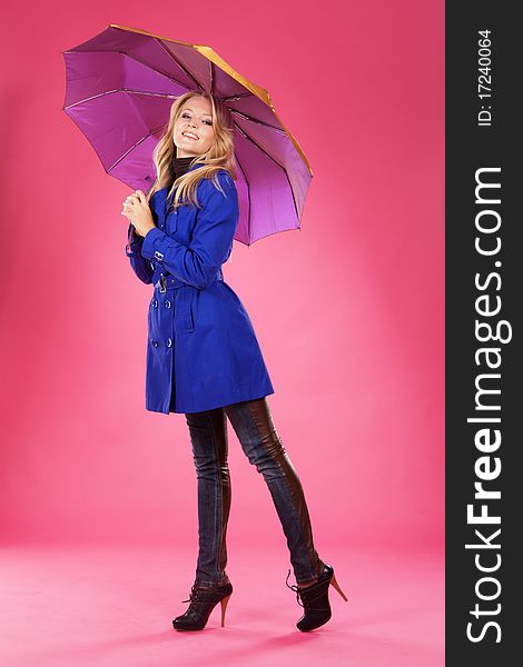 Lovely woman in a blue coat with umbrella against pink background. Lovely woman in a blue coat with umbrella against pink background