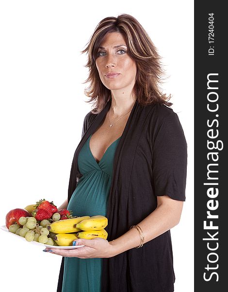 A pregnant woman standing holding a plate of fruit eating healthy for her baby that is in her belly. A pregnant woman standing holding a plate of fruit eating healthy for her baby that is in her belly.