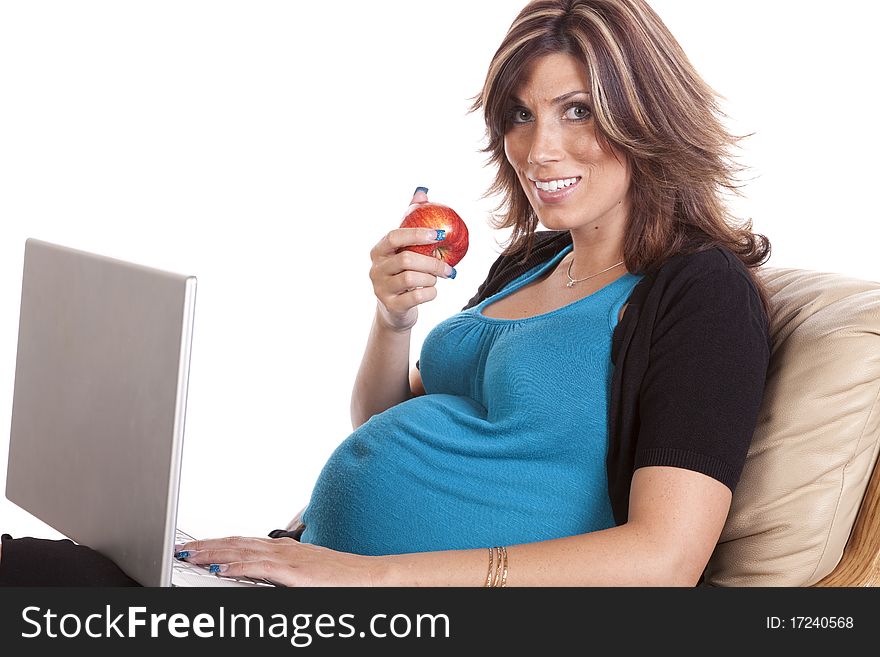 A pregnant business woman sitting and working on her lap top while eating fruit. A pregnant business woman sitting and working on her lap top while eating fruit.