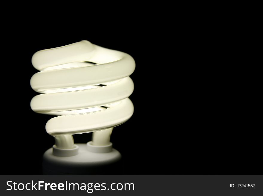 Curly economical environmentally friendly flourescent light bulb that is lighted and on black background. Curly economical environmentally friendly flourescent light bulb that is lighted and on black background