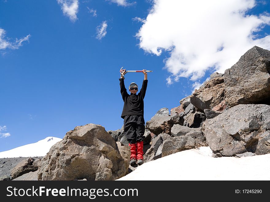 A teenager stands on a mountain with heaved up an above a head ice-axe. A teenager stands on a mountain with heaved up an above a head ice-axe