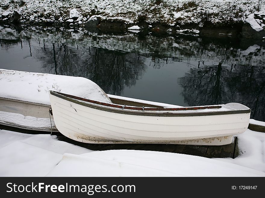 Two rowboats rest in snow on wharf with water and snowy shoreline in background. Two rowboats rest in snow on wharf with water and snowy shoreline in background.