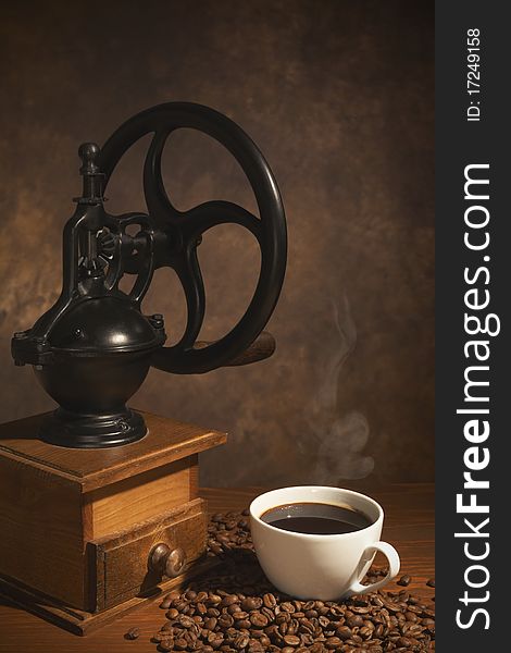 Coffee grinder, a cup of coffee and beans on the table on a brown background