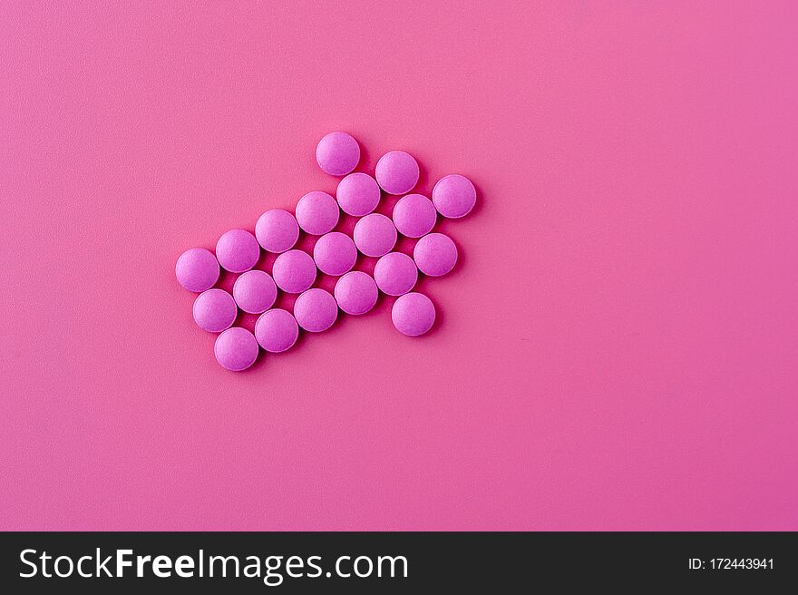 Close-up of pink pills lie on a pink surface depicting an arrow to the right side. Place for advertising. Problem Solving Concept