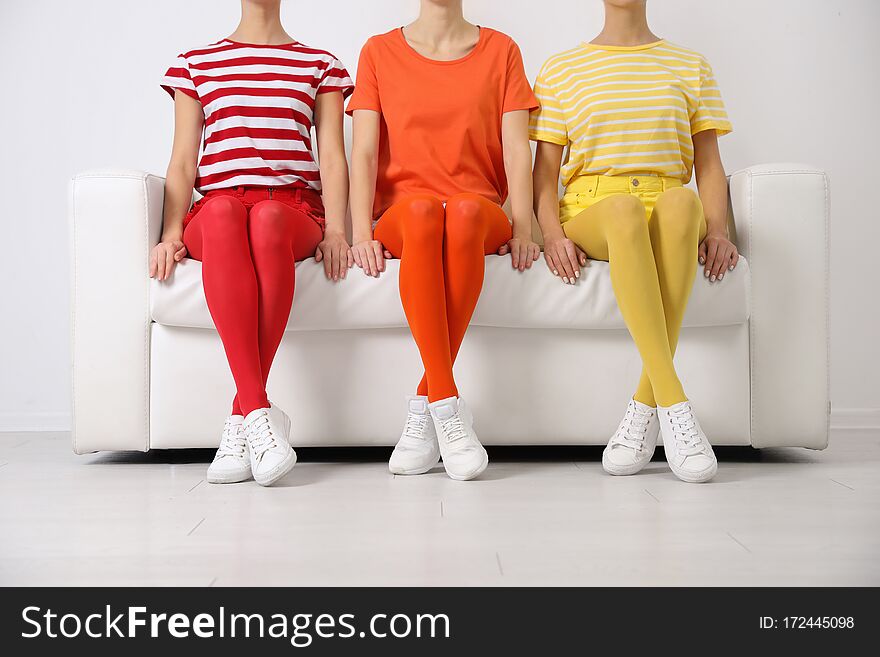 Women wearing bright tights sitting on sofa indoors, closeup