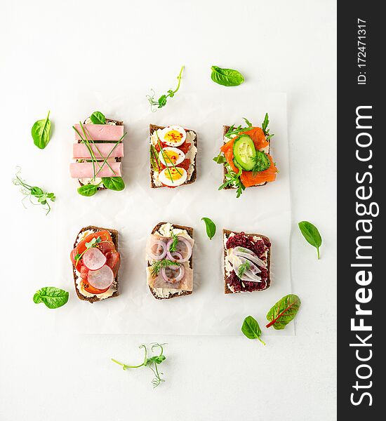 Selection of Danish smorrebrod open sandwiches, green salad leaves on parchment paper on white background. Top view, portrait orientation