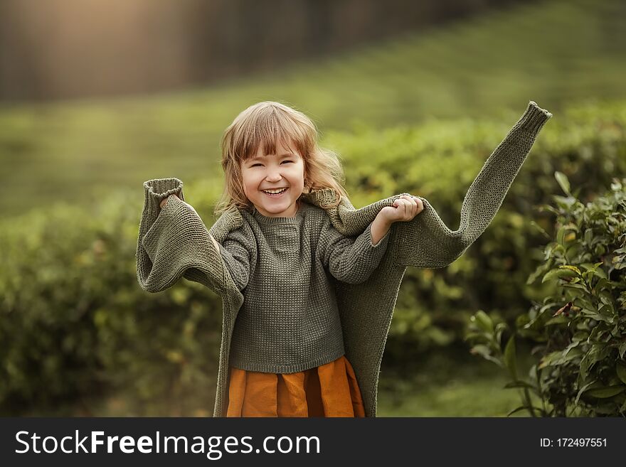 Baby girl in warm clothes in the field with tea tree plants.