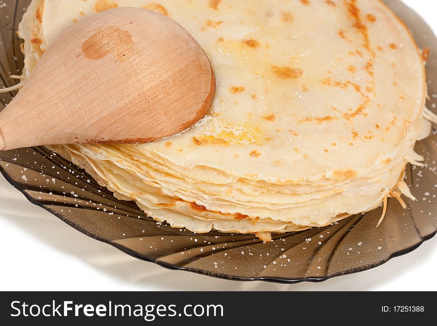 Thin flour traditional Russian pancakes on a plate with a wooden spoon
