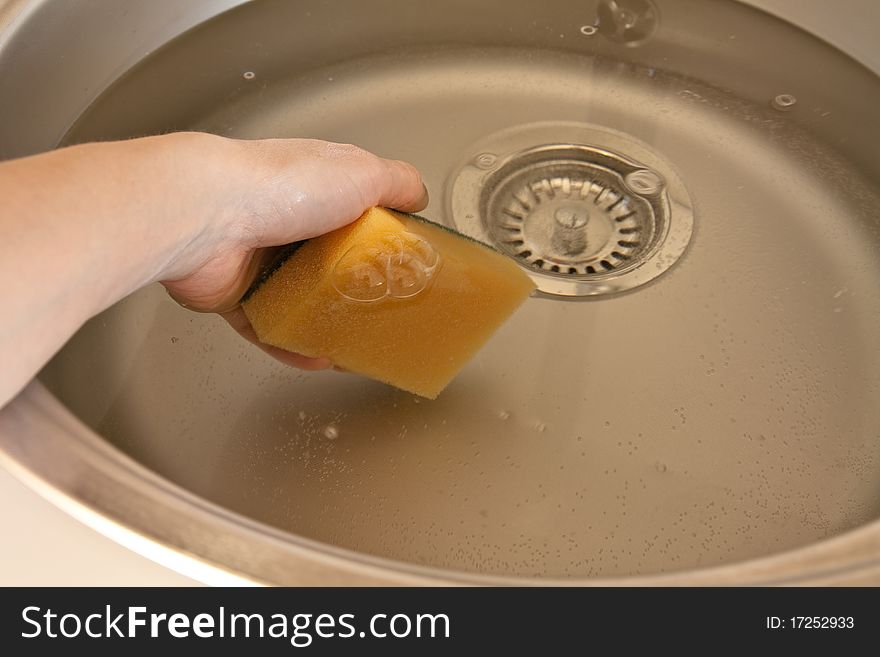 Hand with sponge plunging into the washbasin full of water. Hand with sponge plunging into the washbasin full of water