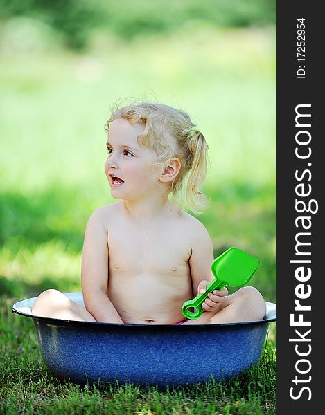 Little girl sits in basin with water. Hot summer day