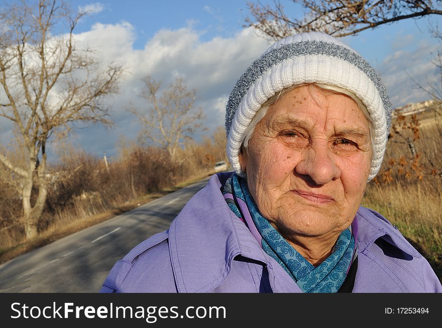 Reflecting an elderly woman in glasses, looks at the camera, the background road, autumn