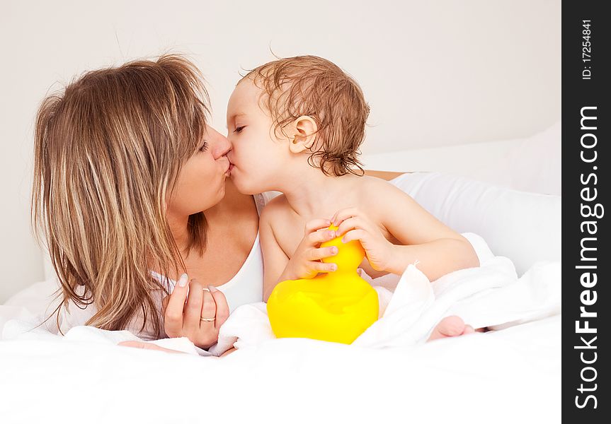 Young beautiful mother and her baby on the bed at home after the shower