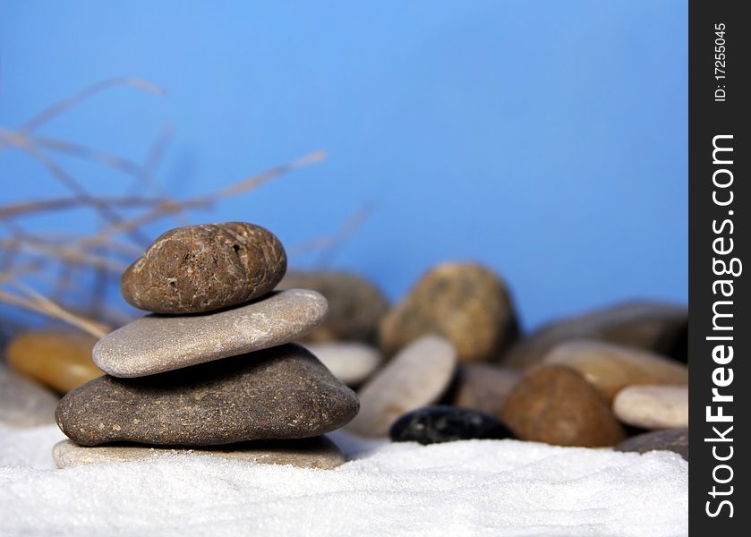 Natural stones stacked on white sand with blue background and grasses. Natural stones stacked on white sand with blue background and grasses