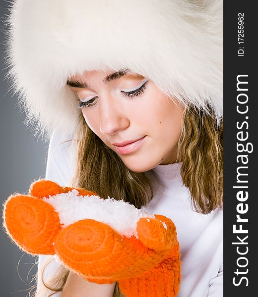 Beautiful winter girl in orange mittens with handful of snow