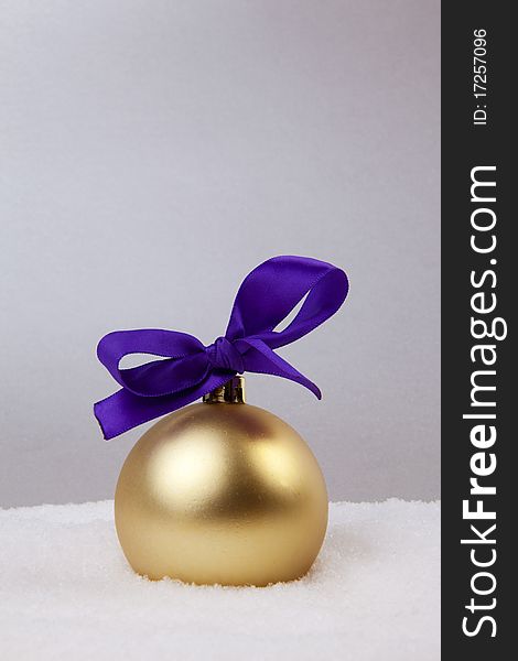 Christmas Golden Ball With Violet Bow And Snow On Silver Background. Christmas Golden Ball With Violet Bow And Snow On Silver Background