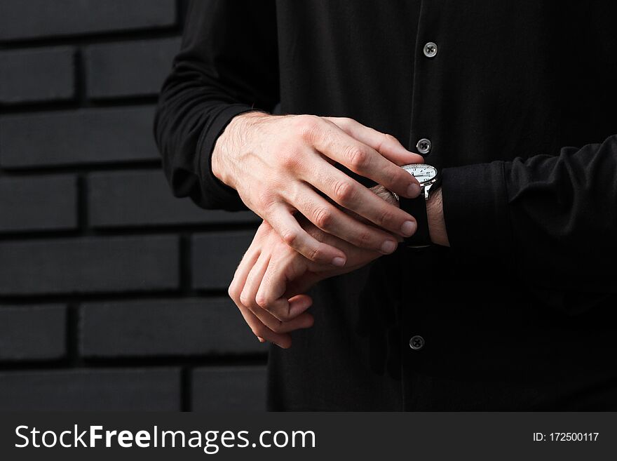 Stylish man with wristwatch near wall checks what hour