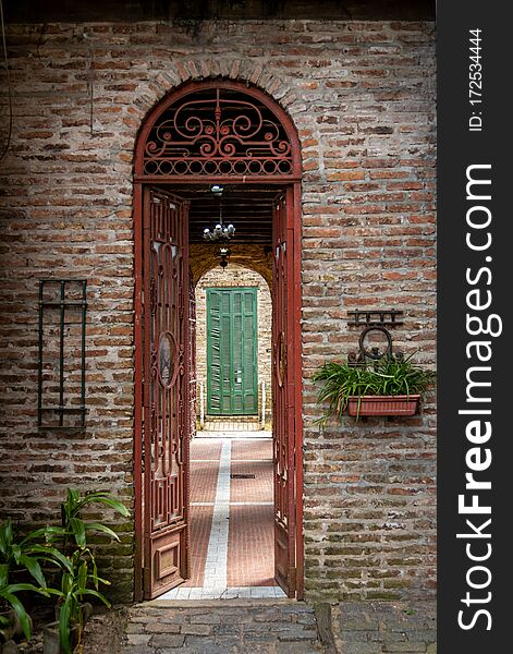 Old brick arch with rusty iron gate open, leading to a passage with a green broken blind at the end of it.