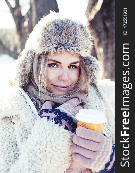 Young pretty teenage hipster girl outdoor in winter snow park having fun drinking coffee, warming up happy smiling, lifestyle people concept close up