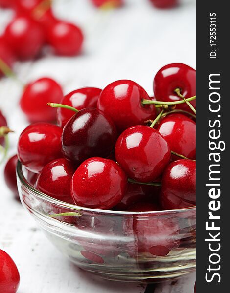 A small glass bowl with ripe fresh cherry on white wooden rustic table