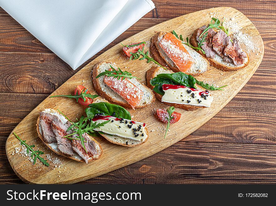 Sandwiches With Red Fish, Beef In Suvit And Soft Cheese. Garnished With Slices Of Microgreen, Arugula And Tomatoes. On A Wooden